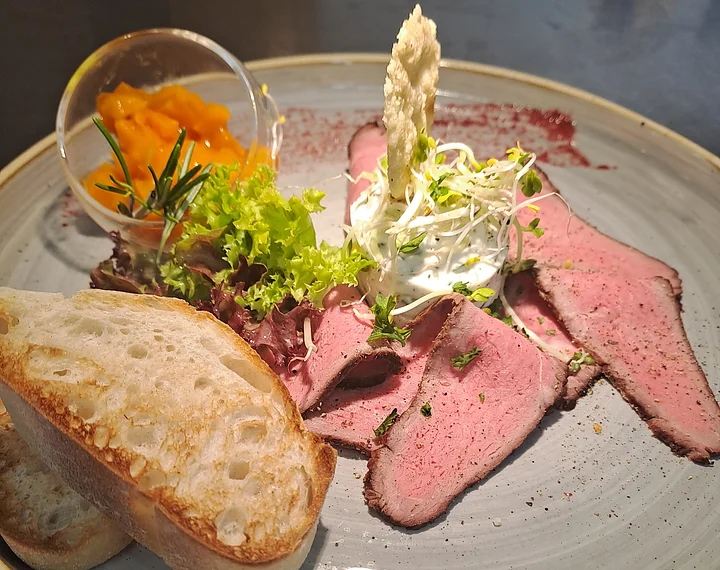 Vorspeise Auerochsen im Landhotel zur Jurahöhe Teller mit Roastbeef, Salat, Brot, Frischkäse mit Sprossen und einem kleinen Glas mit orangener Sauce.