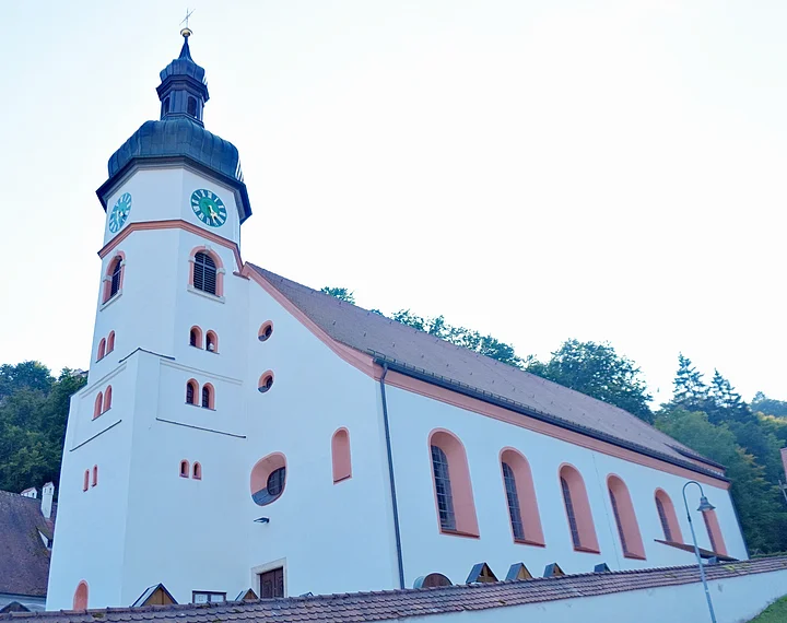 Wellheim Kath. Pfarrei St. Andreas Außenansicht gesamt Kirchturm mit Uhr an weißem Kirchengebäude vor bewaldetem Hügel unter hellem Himmel